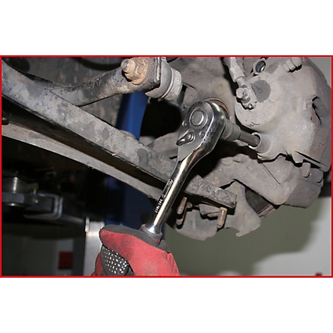 Person mit rotem Handschuh schraubt an einem Autoteil mit einer Ratsche.